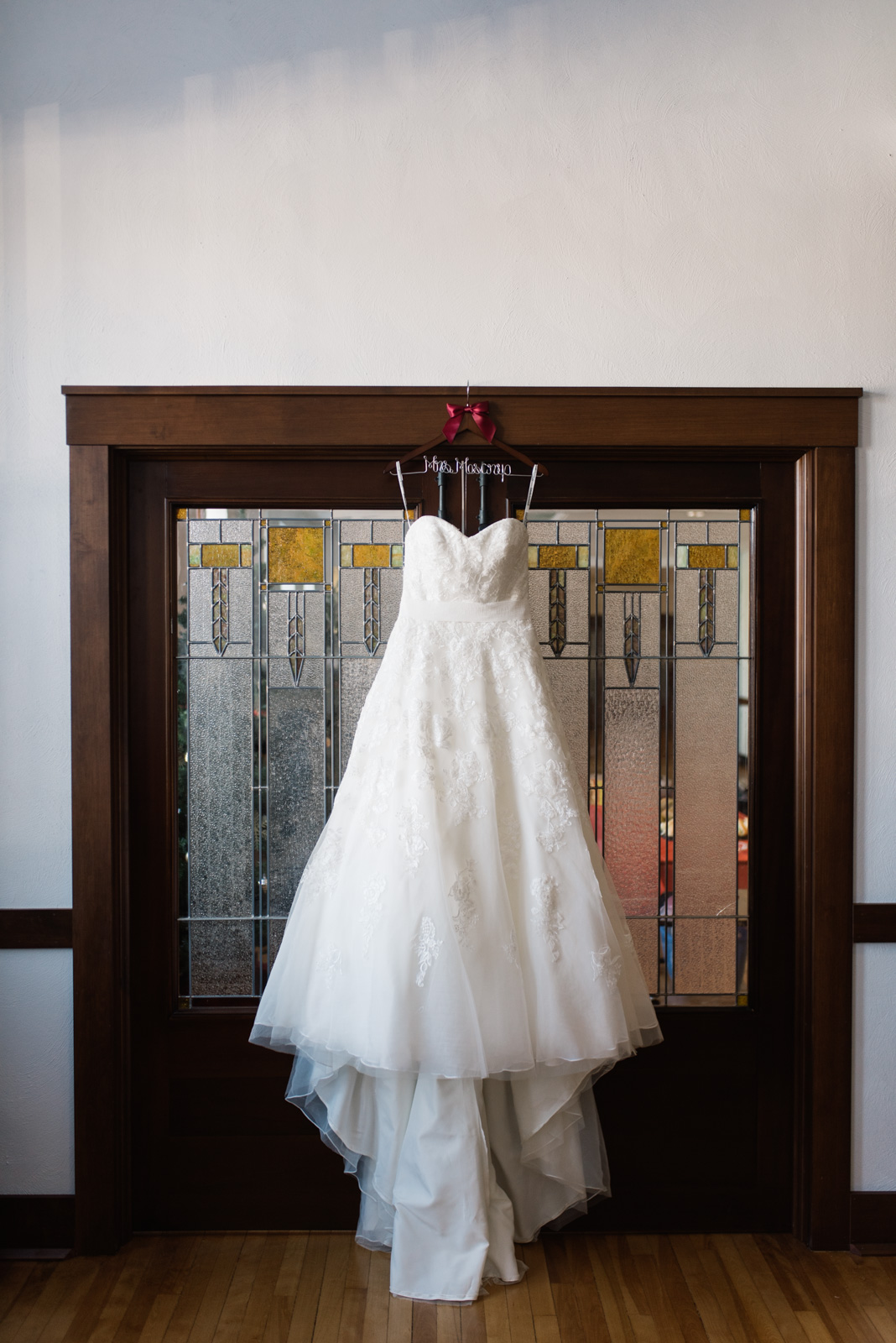 wedding dress hanging on custom wedding hanger in front of stain glass doors