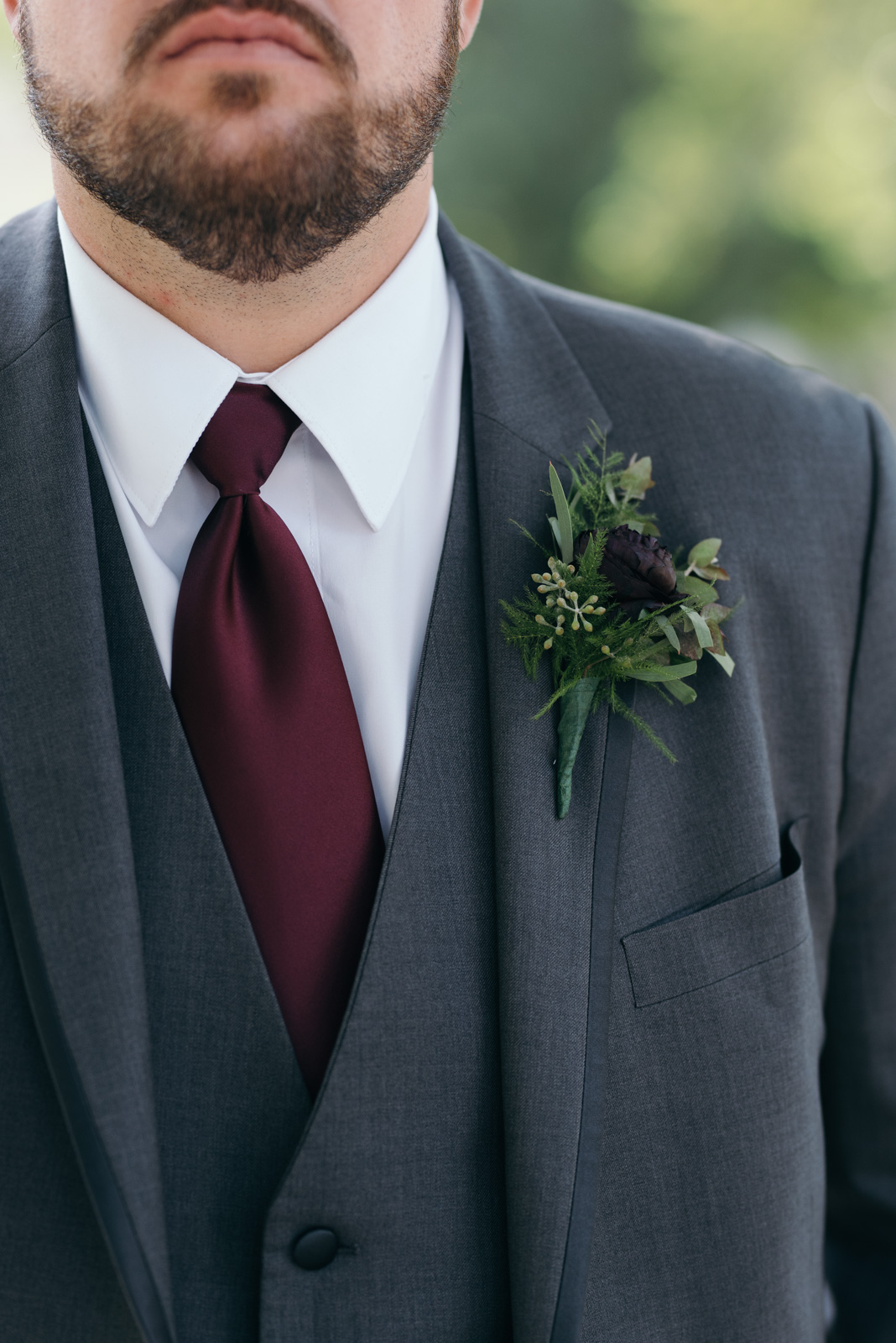 grooms suit with maroon tie and boutonniere