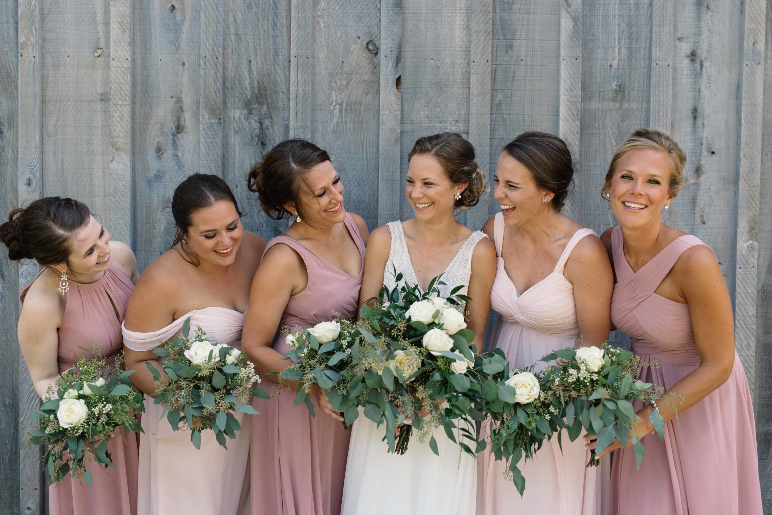 bridesmaids in blush pink dresses laughing with bride gray wood barn schafer century wedding venue