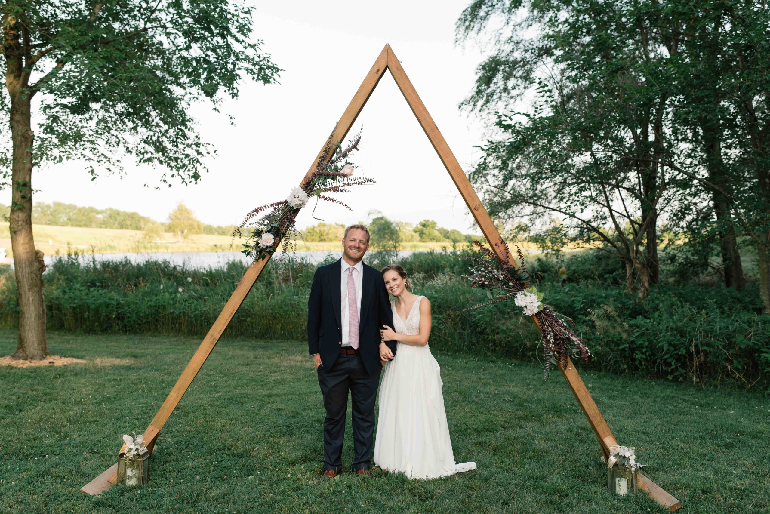 bride and groom snuggle under wooden triangle wedding ceremony arch schafer century barn wedding venue