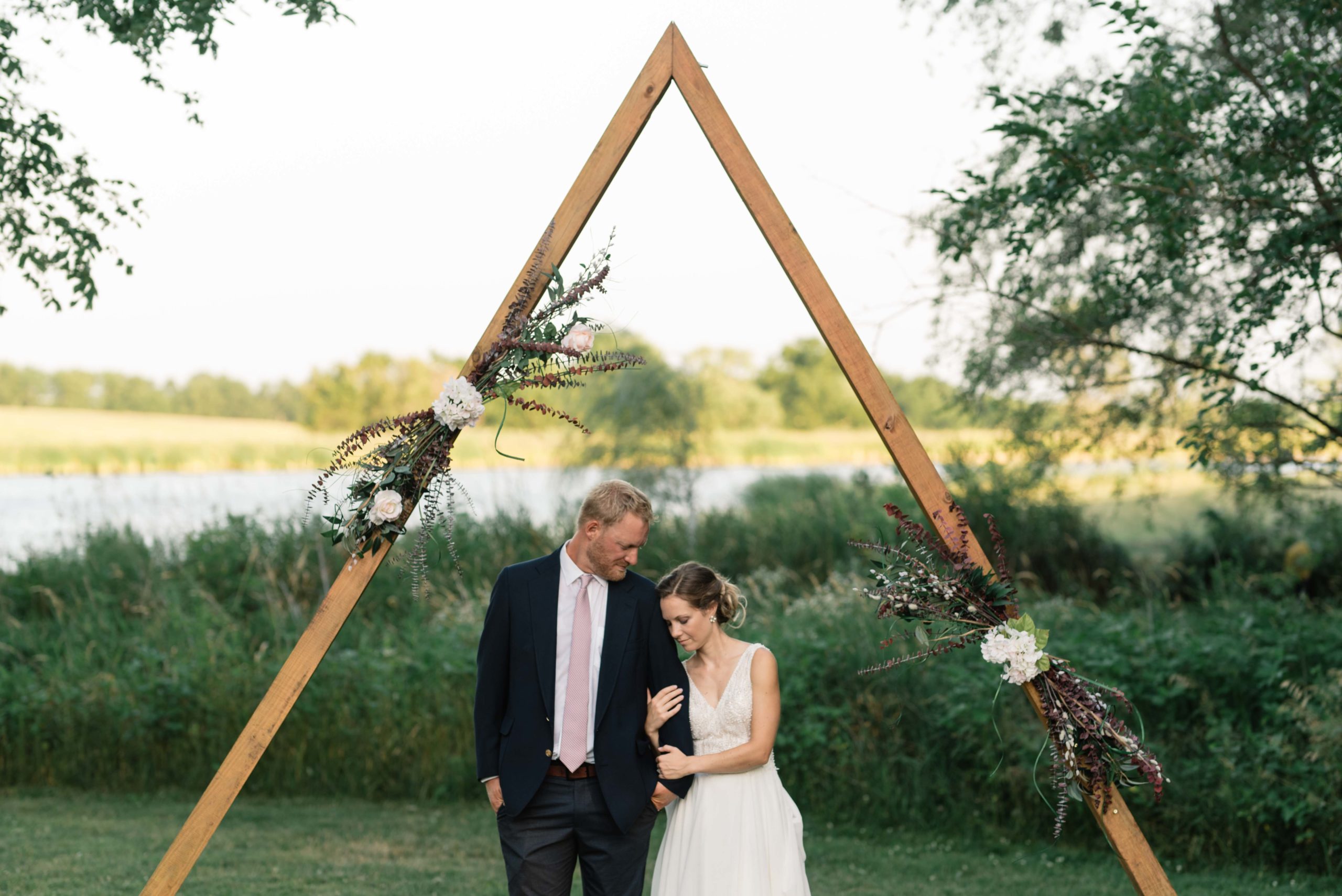 bride and groom snuggle under wooden triangle wedding ceremony arch schafer century barn wedding venue