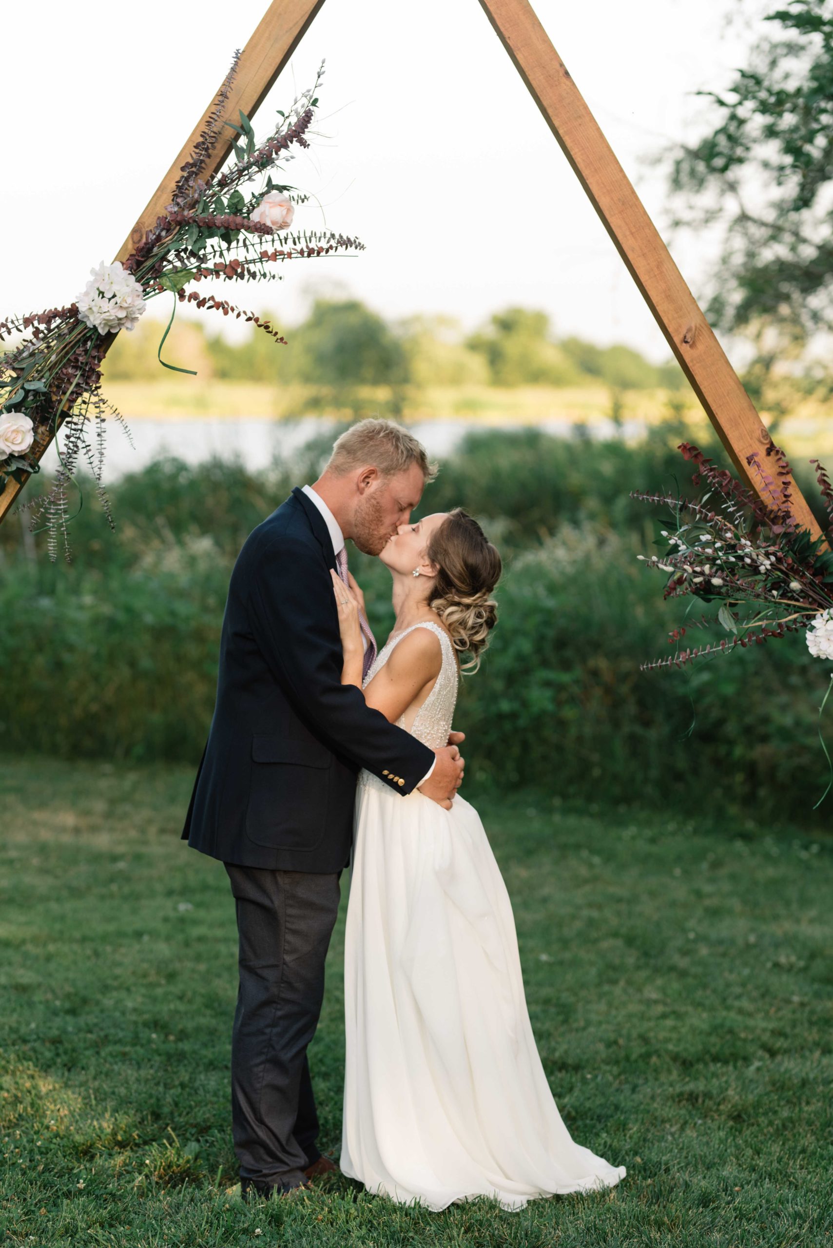 bride and groom snuggle under wooden triangle wedding ceremony arch schafer century barn wedding venue