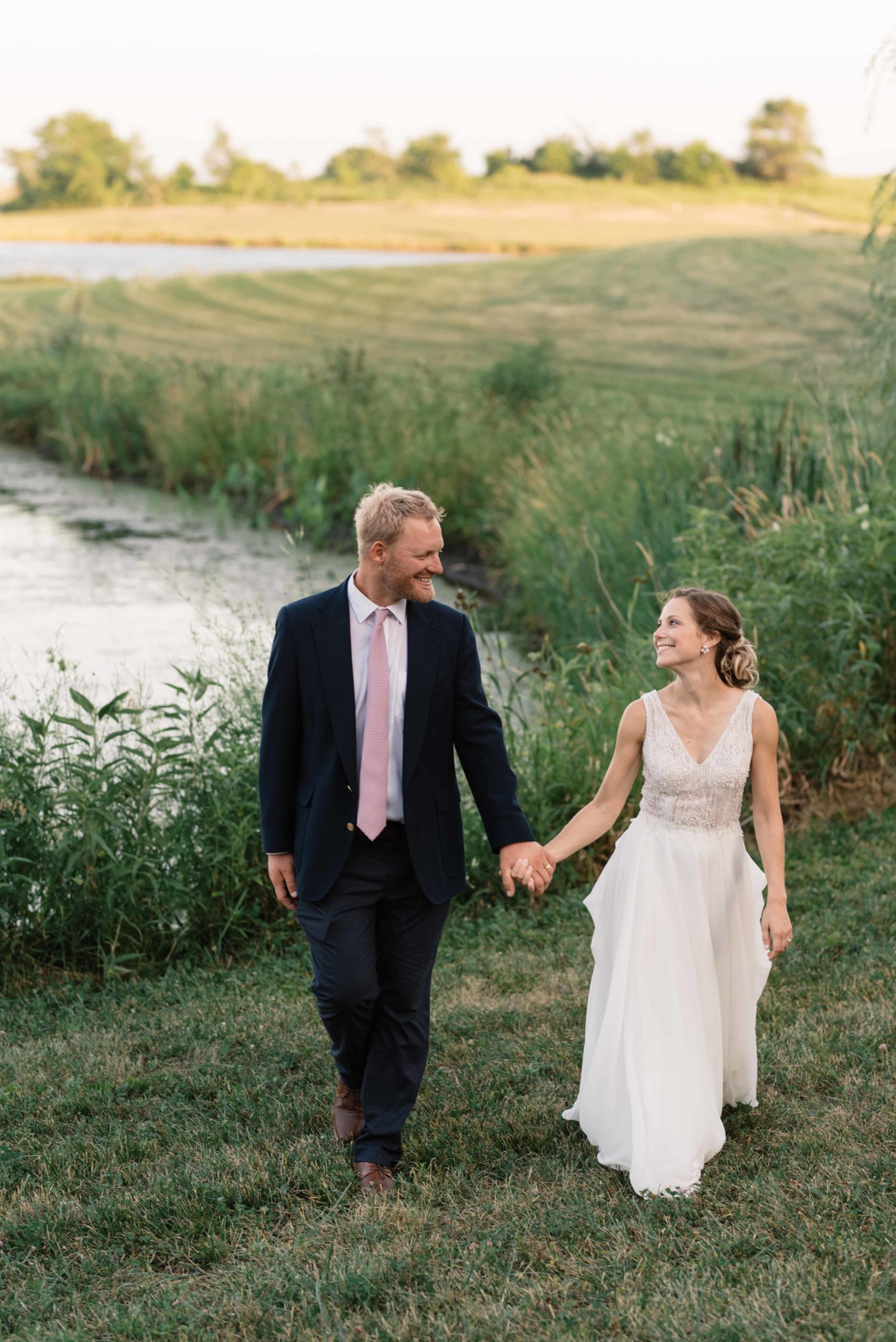 bride and groom holding hands walking near pond at sunset at schafer century barn wedding venue near des moines iowa